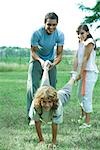 Family outdoors, father and sister holding boy's legs like wheelbarrow