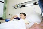 Boy lying in hospital bed, holding toy