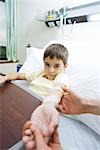 Boy lying in hospital bed, holding out arm