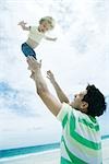 Man throwing child into air on beach