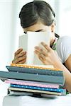Teen girl with stack of homework, hiding face behind book, portrait