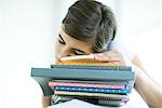 Teen girl resting head on stack of homework, eyes closed