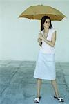 Woman standing under umbrella, full length portrait