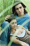 Young couple sitting in grass, woman leaning head against boyfriend's knee