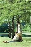 Couple under tree, man sitting on grass while woman stands