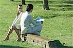 Couple sitting outdoors on low wall, man reading newspaper