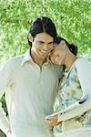 Couple standing outdoors holding newspaper, woman resting head on man's shoulder