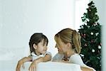 Fille et mère sofa souriant à l'autre, arbre de Noël en arrière-plan