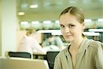 Young woman using laptop in library, smiling at camera