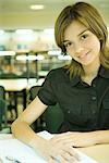 Young woman studying in university library, smiling at camera
