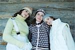 Two sisters and a friend dressed in winter clothes, leaning against log wall, portrait