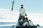 Young snowboarders lying on ground reaching for young man standing behind them