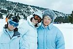 Senior woman with teen and preteen granddaughters, wearing coats and hats, standing in snowy landscape