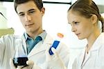 Young male and female scientists holding test tube and flask