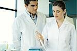 Female lab worker holding dropper, male colleague watching her