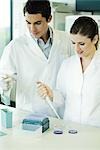 Female lab worker dropping solution into Petri dish, standing next to male colleague