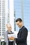 Two business associates standing outdoors, looking at file together, waist up