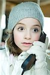Girl using phone, dressed in winter clothing, looking away with wide eyes