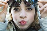 Preteen girl lifting sunglasses, puckering at camera, close-up