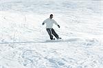 Young man snowboarding down ski slope, full length