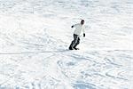 Young man snowboarding down ski slope, full length