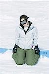 Teenage girl kneeling in snow with snowboard, looking at camera