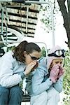 Teenage girls sitting on chair lift together, leaning over, shouting