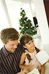 Father and daughter opening present together, Christmas tree in background