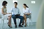 Drei Geschäftspartner sitzen auf Stühlen, Dokumente auf runden halten, reden