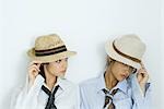 Two young friends pulling hats down over their faces, one looking at camera, portrait