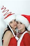 Two young female friends dressed in Christmas costumes, cheek to cheek, smiling at camera, portrait