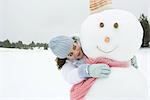 Female embracing snowman, smiling, portrait