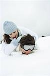 Young couple lying on the ground in snow, one on top of the other, smiling