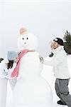 Young couple peeking around snowman at each other, holding up snowballs