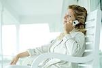 Woman sitting on porch using cell phone, smiling, looking away