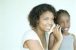 Mother holding cell phone up to daughter's ear, both smiling, daughter looking at camera