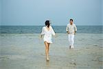 Man and young female companion on beach, walking toward camera, man in background, full length