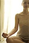 Teenage girl in front of window sitting in lotus position, eyes closed, cropped view