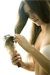 Young woman in bra brushing hair, cropped side view