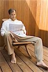 Man sitting in lounge chair reading newspaper