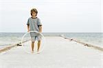 Boy standing on pier playing with plastic hoop, full length