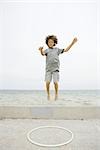 Boy jumping off low wall toward plastic hoop, arms raised