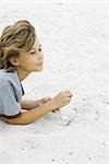 Boy lying in sand, looking away, side view