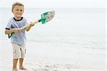 Young boy holding up shovel and throwing sand, smiling at camera