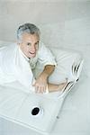 Mature man lying on chaise longue holding book, looking up at camera, high angle view