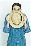 Teenage girl hiding behind straw hat, looking at camera