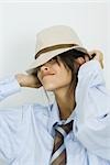 Teenage girl wearing tie, putting on hat, smiling at camera