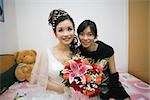 Bride sitting on bed with female friend, smiling, portrait