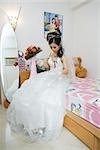 Bride sitting on bed, looking down at dress, full length