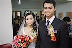 Bride and groom wearing corsages, smiling at camera, friends and family in background